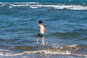 Boy Jumping In Sea Waves with Water Splashes. Concept of summer vacation