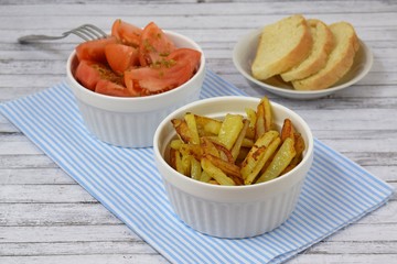 Delicious fried potatoes and fresh tomatoes in white dishes on the table.