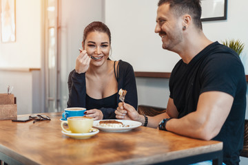 Young couple sitting in cafe at date, drinking coffee and eating dessert.