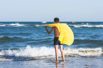 Back view on the boy standing on seashore of the beach in the yellow towel  and looking on the sea....