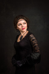 Close up. Roaring Twenties. Woman portrait in the style of Gatsby. Low key. Beautiful young woman in a black dress, satin gloves and a black fur cape.