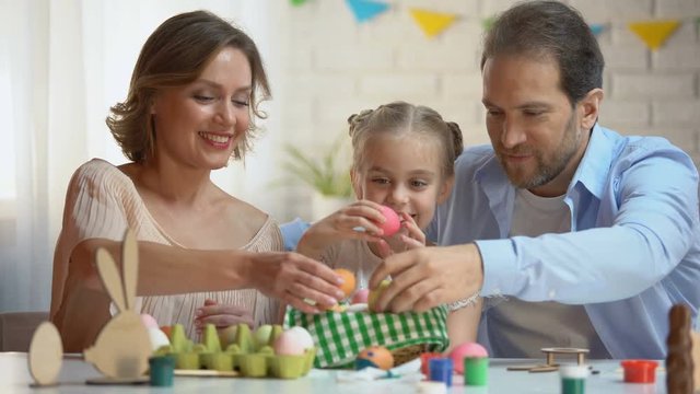 Beautiful family putting dyed Easter eggs into basket, Christians traditions