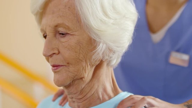 Unrecognizable female physiotherapist massaging shoulders and back of elderly woman with grey hair