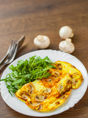 Omelet with mushrooms and arugula salad in white plate on wooden table background.
