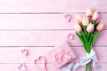 Valentines day and love concept. Pink paper hearts with gift box and tulips with ribbon on pink pastel wooden background.