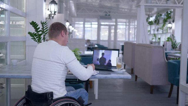 online education, mature learner crippled in wheel chair writes notes in a notebook while watching training sitting at a table in a restaurant