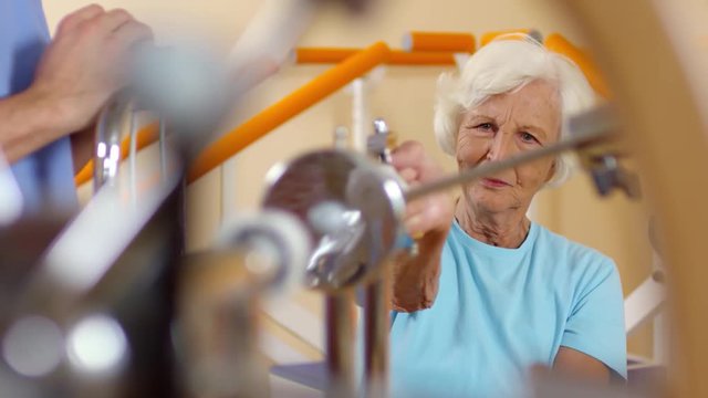 Medium shot of elderly woman with grey hair using rotating wrist exerciser at physiotherapy session