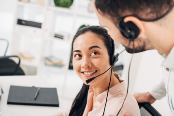 attractive call center operator smiling and looking at colleague in office