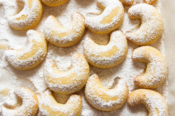 German and Austrian traditional Christmas cookies vanilla crescents on white tray powdered with castor sugar. Beautiful light. Top view. Food pattern. Holiday baking concept