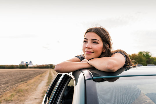 Smiling young woman looking out of sunroof of a car