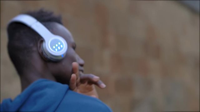 young american african man listening music with headphones and dancing-outdoor