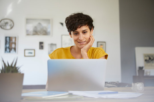Portrait of smiling woman at home sitting at table using laptop