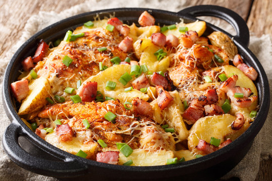 Delicious homemade baked chicken fillet with potatoes, bacon and cheese close-up in a frying pan. horizontal