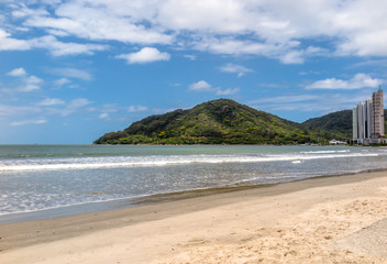Fototapeta na wymiar View from the right side of the Balneário Camboriú Central Beach, with a hill in the background and blue sky with clouds, Santa Catarina