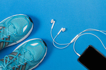 Zapatillas de deporte sobre fondo azul con teléfono móvil y auriculares. Vista superior. Copy space