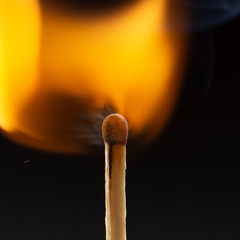 Burning wooden match with a red match head on a black background.