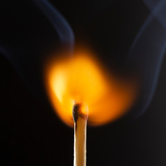 Burning wooden match with a red match head on a black background.