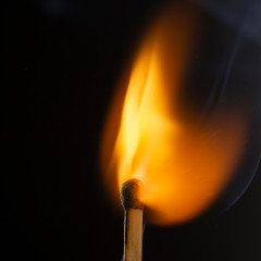 Burning wooden match with a red match head on a black background.
