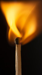 Burning wooden match with a red match head on a black background.