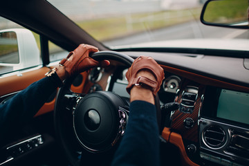 The hands of the driver in leather gloves, driving a moving car.