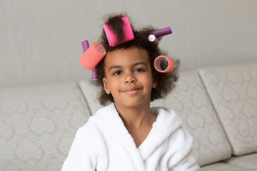 Happy little afro american woman with hair curlers. Beautiful black girl with hairpins in her hair...