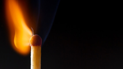 Burning wooden match with a red match head on a black background.