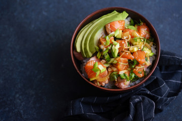 Poke bowl with raw marinated salmon, cucumbers and avocado on dark blue concrete background