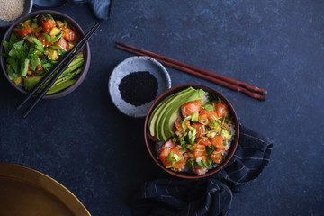Poke bowl with raw marinated salmon, cucumbers and avocado on dark blue concrete background