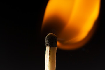Burning wooden match with a red match head on a black background.