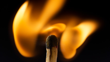 Burning wooden match with a red match head on a black background.