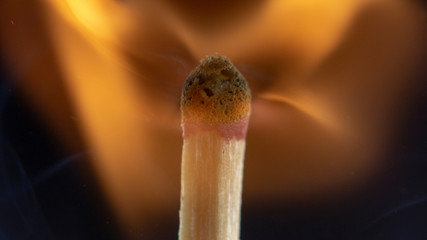 Burning wooden match with a red match head on a black background.