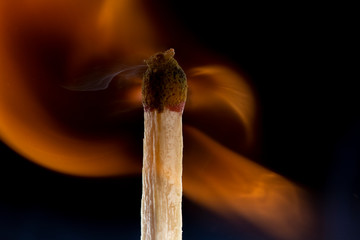 Burning wooden match with a red match head on a black background.
