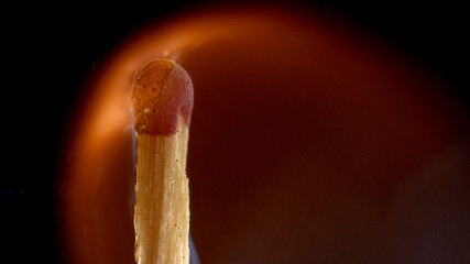Burning wooden match with a red match head on a black background.