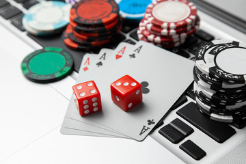 Online casino laptop. Laptop keyboard and chips with dice and playing cards on a green gaming table. Game addiction gambling. Poker online