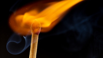 Burning wooden match with a red match head on a black background.