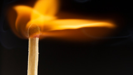 Burning wooden match with a red match head on a black background.