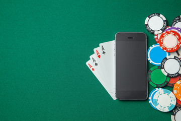 Mobile phone casino online. Mobile phone and game cards with chips  on green gaming table. Gambling addiction in cracking games. Poker online. Copy space for text.