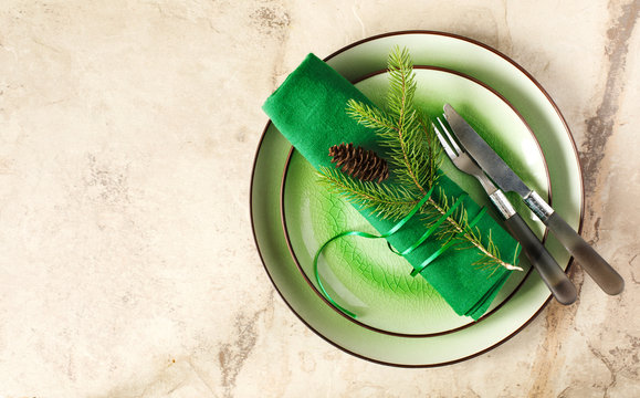 Two green empty round plates with napkin, fork and knife and Christmas decoration - fir tree brunch and cones, top view. Christmas menu background