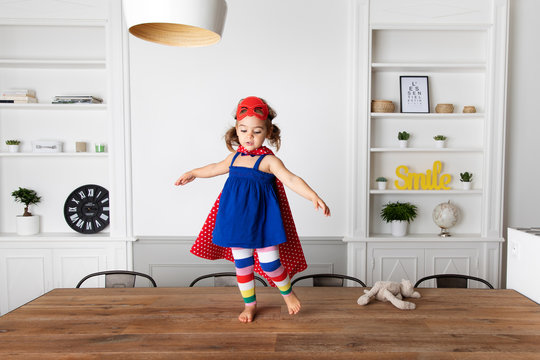 Little girl dressed up as superhero standing on kitchen table