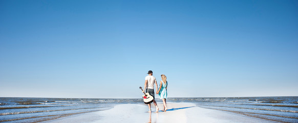 young couple in love with a guitar on the seashore.