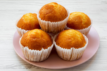 Fresh muffins on pink plate on a white wooden background, side view. Closeup.