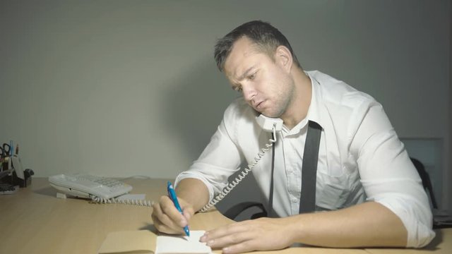 The guy detective in a white shirt listens to the interlocutor with a surprised face in his office