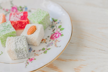 Traditional turkish delight on a plate on white wooden background. Assorted Oriental sweets.
