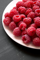Fresh organic raspberry on a pink plate on black surface, low angle view. Closeup.