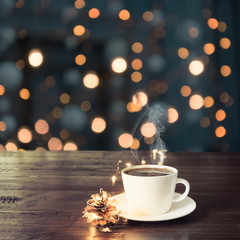 Fototapeta premium Cup of black coffee on wooden table in cafe. Christmas lights and gold garland on background.