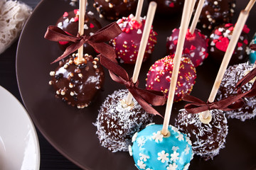 Various cake pops decorated with white and dark chocolate on a brown background