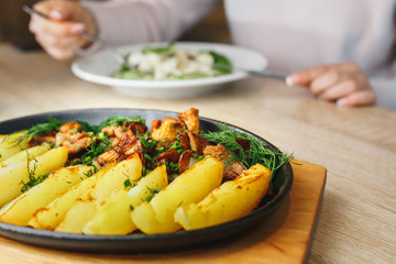 Fried potato with mushrooms chanterelle. beautifully rustic in a black plate rustic on a wooden table.