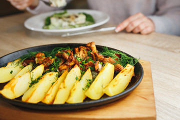 Fried potato with mushrooms chanterelle. beautifully rustic in a black plate rustic on a wooden table.