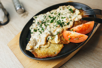 Plate with tasty potato pancakes with tomatoes and gravy on wooden table