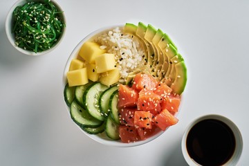 Raw Organic Poke Bowl with salmon, avocado, rice, mango, cucumbers, chuka salad and soy sauce...